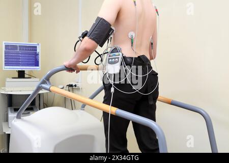 Patient mit EKG-Elektroden auf dem Rücken und einem Instrument zur Blutdruckmessung bei Belastung auf dem Laufband Stockfoto