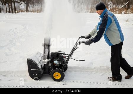 Der Mensch entfernt Schnee mit einer Gasschneewerfer am Wintertag. Stockfoto