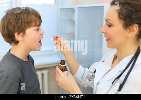 Gesundheitspersonal in weißem Kleid, das dem Patienten im Löffel Medizin gibt, Fokus auf Jungen Stockfoto