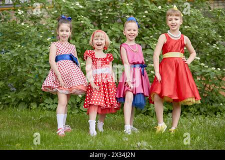 Vier lächelnde kleine Mädchen in Tanzanzügen posieren auf dem Rasen. Stockfoto