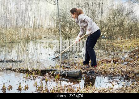 Junge Frau zieht Müll aus schmutzigem Wasser während der Frühjahrsputz des Gebiets. Stockfoto