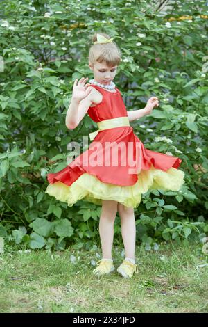 Kleines Mädchen in rotem Kleid mit gelbem Unterrock dreht sich im Freien. Stockfoto