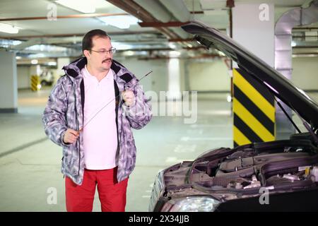 Der Mann in der Brille, der auf den Messstab in der Nähe des Autos in der Tiefgarage schaut Stockfoto