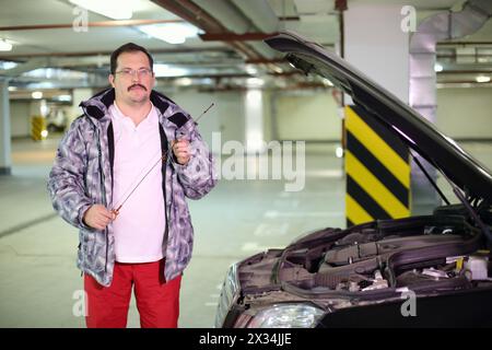 Der Mann mit Brille überprüft den Ölstand in einem Automotor in der Tiefgarage Stockfoto