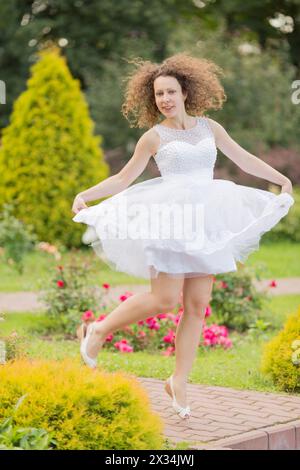 Vollständiges Porträt einer schönen tanzenden Frau in weißem Kleid im Sommerpark Stockfoto