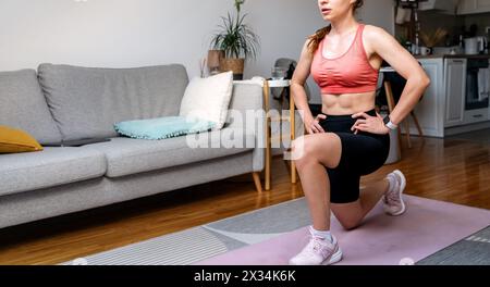 Sportliche Frau in Sportbekleidung, die in ihrer Wohnung trainiert. Aktiver Lebensstil und Fitness zu Hause. Bauchmuskeln. Stockfoto