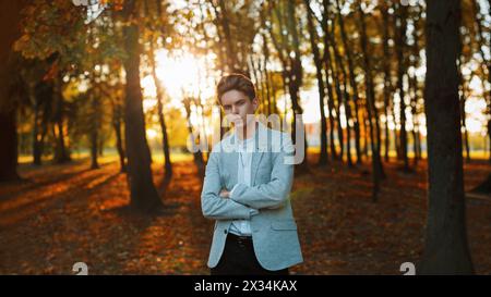 Junger, gutaussehender Kerl in stylischer Jacke und Hemd, der bei Sonnenuntergang im Park steht. Stockfoto