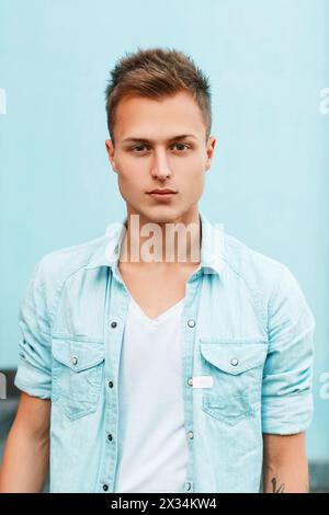 Nahaufnahme Porträt Eines jungen, stylischen Mannes in Einem Denim-Shirt in der Nähe Einer blauen Wand. Stockfoto