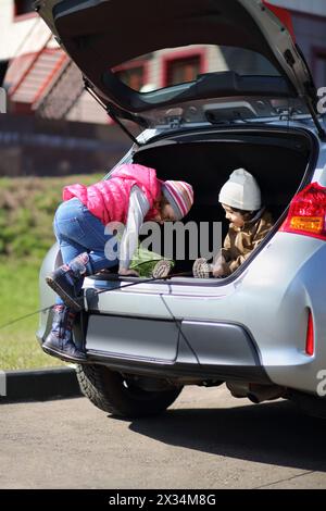 Kleines Mädchen und Junge spielen im offenen Kofferraum eines fremden Autos Stockfoto