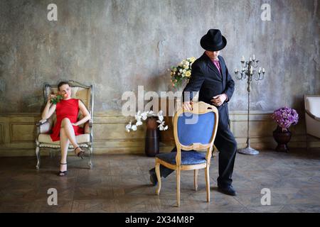 Frau mit Rose sitzt auf dem Stuhl und sieht den Mann an, der mit dem Stuhl tanzt Stockfoto