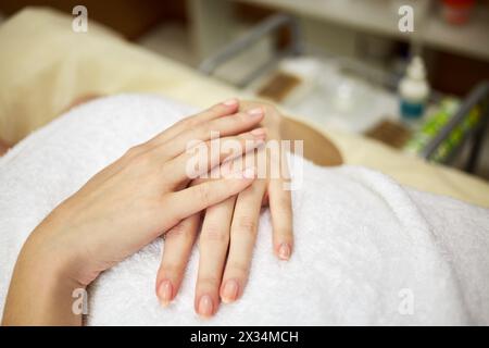 Hände einer Frau in Handtuch gewickelt und auf dem Rücken auf der Couch im Schönheitssalon liegend. Stockfoto