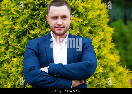 Unrasierter, gutaussehender Mann in Hemd und blauer Jacke posiert im grünen Sommergarten Stockfoto