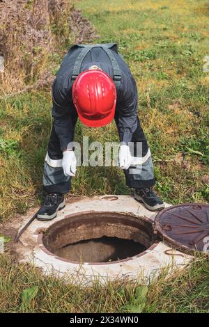 Ein Arbeiter schaut in einen septischen Kanal und überprüft auf Wasseransammlungen. Sanitär- und Sanitärarbeiten. Stockfoto