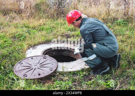 Übertragung der Messwerte des Wasserzählers. Ein Gemeindearbeiter inspiziert einen Wasserzähler in einem Brunnen und überprüft die Messwerte. Stockfoto