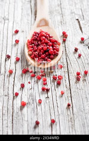 Holzlöffel mit rosa Pfeffer isoliert auf rustikalem Hintergrund Stockfoto