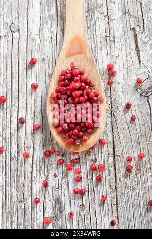 Holzlöffel mit rosa Pfeffer isoliert auf rustikalem Hintergrund Stockfoto