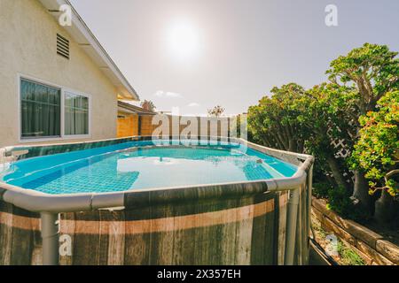 Hinterhof mit einem oberirdischen Pool und üppigen grünen Pflanzen an einem sonnigen Tag. Stockfoto