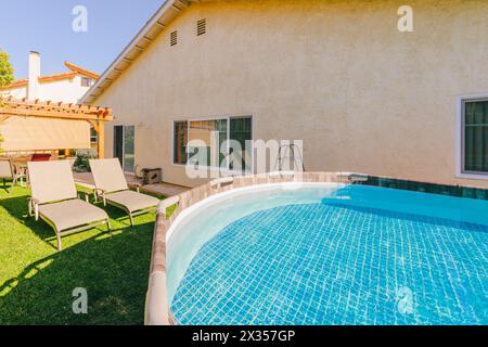 Zwei Liegestühle in einem Hinterhof mit Blick auf einen überirdischen Pool an einem hellen, sonnigen Tag. Stockfoto