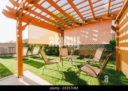 Gemütliche Sitzgelegenheiten im Freien unter einer hölzernen Pergola mit Ambiente-Beleuchtung in einem Garten. Stockfoto