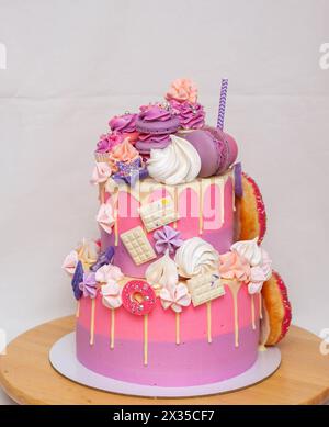 Rosa Ombre Geburtstagskuchen mit Donuts, Baisons und Schokolade auf neutralem Hintergrund. Cupcake oben Stockfoto