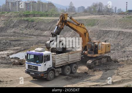 Der Bagger lädt ausgehobenen Boden in einen großen Lkw in einem bewohnten Gebiet Stockfoto