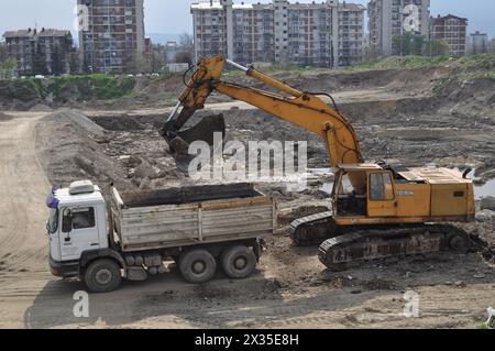 Der Bagger lädt ausgehobenen Boden in einen großen Lkw in einem bewohnten Gebiet Stockfoto