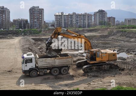 Der Bagger lädt ausgehobenen Boden in einen großen Lkw in einem bewohnten Gebiet Stockfoto