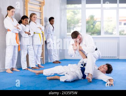 Judo-Trainer zeigt Kampftechniken im Sparring mit einem Jungen für eine Gruppe junger Athleten Stockfoto