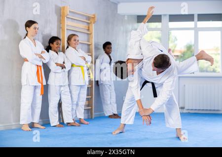 Judo-Trainer zeigt Kampftechniken im Sparring mit einem Jungen für eine Gruppe junger Athleten Stockfoto