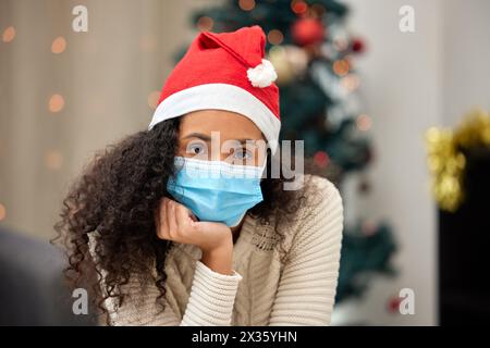 Weihnachten, medizinische Maske und Porträt der Frau im Wohnzimmer für Pandemie, Lockdown oder Selbstisolierung zu Hause. Weihnachten, Quarantäne und traurige Person mit Stockfoto