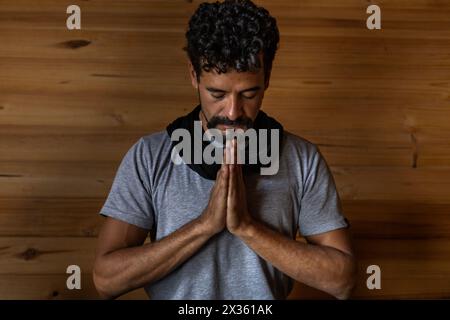 Vorderansicht eines jungen lateinamerikanischen Mannes in Meditationsposition. Hintergrund der Holzlatten. Konzept von Wellness und Yoga. Stockfoto