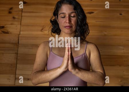 Vorderansicht einer jungen lateinamerikanischen Frau in Meditationsposition. Hintergrund der Holzlatten. Konzept von Wellness und Yoga. Stockfoto