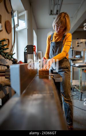 Fokussierte Zimmerfrau, die an einem Elektrohobel arbeitet und eine Schutzbrille mit Spezialausrüstung trägt. Stockfoto