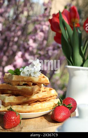 Frisch gebackene Waffeln und ein wunderschöner Tulpenstrauß auf dem Tisch im Garten, Nahaufnahme Stockfoto