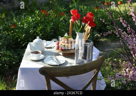 Wunderschöner Tulpenstrauß und frisch gebackene Waffeln auf dem Tisch, serviert zum Teetrinken im Garten Stockfoto