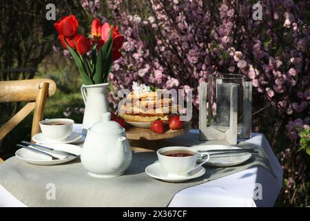 Wunderschöner Tulpenstrauß und frisch gebackene Waffeln auf dem Tisch, serviert zum Teetrinken im Garten Stockfoto