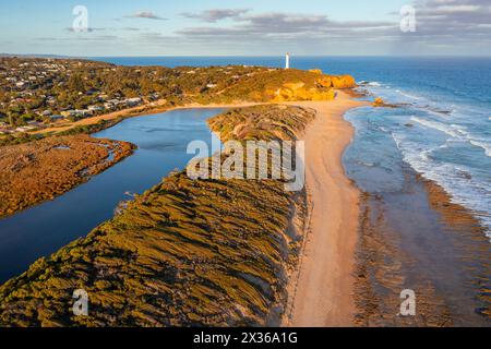 Aus der Vogelperspektive auf einen Bach, der entlang der Küste verläuft, mit einem entfernten Leuchtturm am Aireys Inlet an der Great Ocean Road in Victoria, Australien. Stockfoto