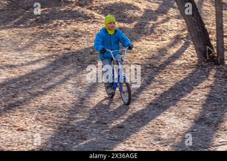 Der siebenjährige Junge fährt im Herbstpark Fahrrad. Ein Junge in blauer Jacke und gelbem Hut radelt durch einen Park Stockfoto