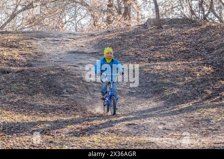 Der siebenjährige Junge fährt im Herbstpark Fahrrad. Ein Junge in blauer Jacke und gelbem Hut radelt durch einen Park Stockfoto