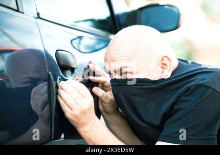 Nahaufnahme Dieb, der ein Auto klaut. Ein nicht verschlossenes Auto, ein Mann, der in das Innere einbrechen will. Der Mann in schwarz gekleidet mit einer Sturmhaube auf dem Kopf, der versucht einzubrechen Stockfoto