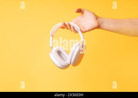 Die Hand hält weiße kabellose Kopfhörer vor gelbem Hintergrund Stockfoto