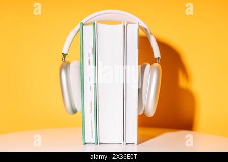 Weiße kabellose Kopfhörer auf einem Stapel Bücher vor gelbem Hintergrund Stockfoto