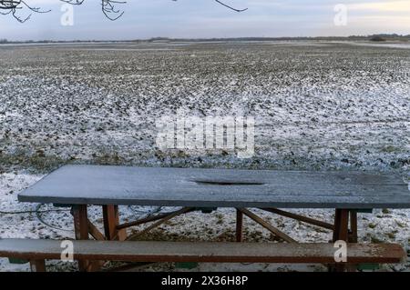 Eine handgefertigte Holzbank und ein Tisch und ein endloses Ackerland im Hintergrund, bedeckt mit Schnee Stockfoto