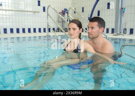 Schwangere Frau mit Partner, die sich im Schwimmbad entspannen Stockfoto