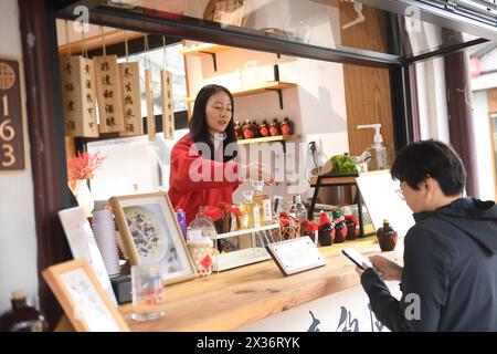 (240425) -- SHAOXING, 25. April 2024 (Xinhua) -- Ein Angestellter führt einen Kunden an, über ihr Mobiltelefon für Kaffeespezialitäten mit gelbem Reiswein in einem Geschäft in der Cangqiao Straight Street in Shaoxing, ostchinesische Provinz Zhejiang, 20. Februar 2024 zu bezahlen. Cangqiao Zhijie, wörtlich übersetzt als „Cangqiao Straight Street“, ist eine historische und kulturelle Stätte mit alten Häusern von einzigartigem Stil. Auf einer Fläche von 0,064 Quadratkilometern konnte die 1.500 Meter lange Straße bis in die Song-Dynastie (960–1279) zurückverfolgt werden. Seit den 1990er Jahren werden hier Sanierungs- und Schutzmaßnahmen durchgeführt Stockfoto