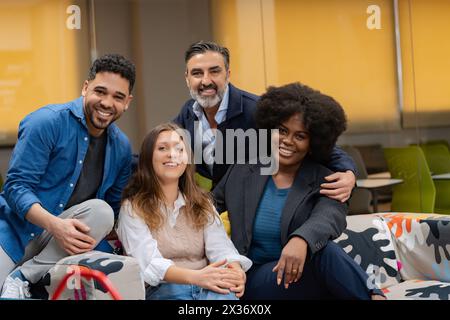Ein vielseitiges Team glücklicher Kollegen posiert gemeinsam auf einem bunten gemusterten Sofa in einem kreativen Bürobereich. Stockfoto