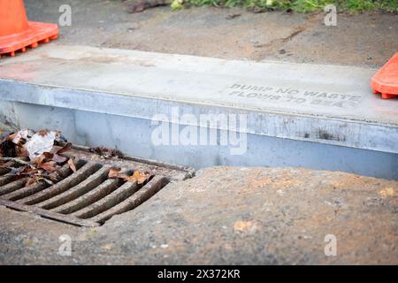 Abdeckung des Abflussgitters am Straßenrand. Müllkippe kein Abfallfluss zum Meer, aufgedruckt auf der Betonaufkantung über der Abflussabdeckung. North Shore; Auckland. Stockfoto