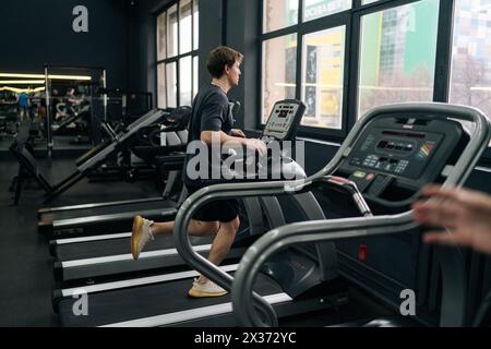 Rückansicht des sportlichen Mannes, der auf einem Fitnessgerät joggt und in einem gut ausgestatteten Fitnessclub Cardio-Training absolviert. Seitenansicht eines Sportanfänger mit Stockfoto