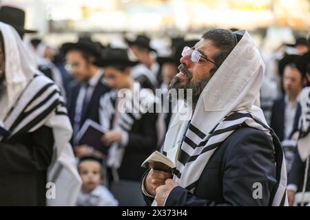 Jerusalem, Israel. April 2024. Ein jüdischer Mann, der mit einem Tallit bedeckt ist, ein Gebetsbuch (Sidur) hält, steht unter anderem und betet sehr emotional an der Wailing Wall Credit: Yoram Biberman/Alamy Live News. Stockfoto