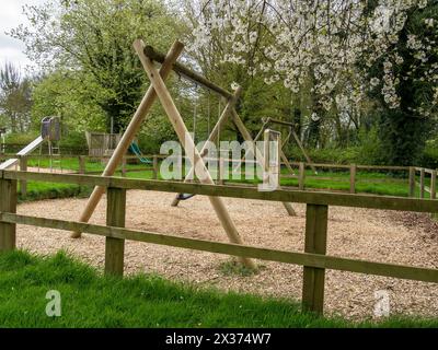 Umzäunter Kinderspielplatz/Erholungsbereich/Spielplatz mit Schaukeln und Rindenspänen darunter, Somerby, Leicestershire, England, Großbritannien Stockfoto